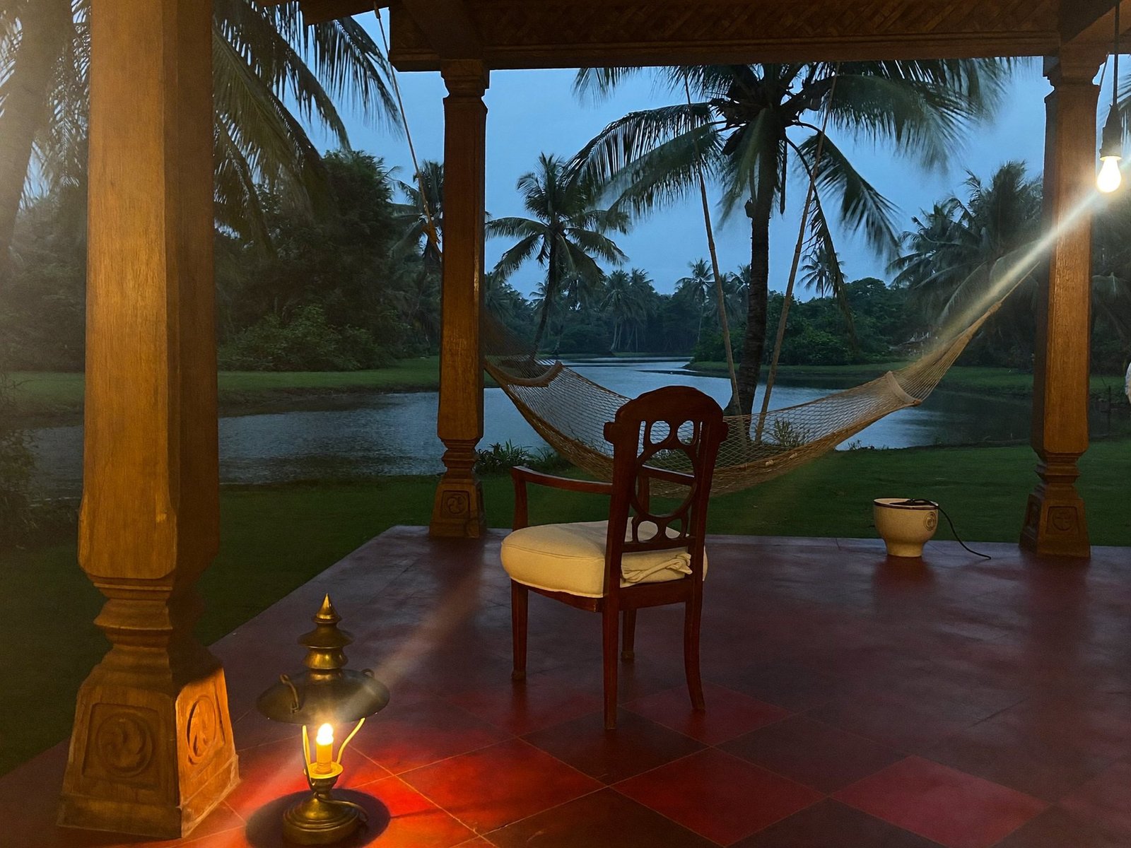 The veranda at dusk with a lamp lit and a hammock looking out to the paddy