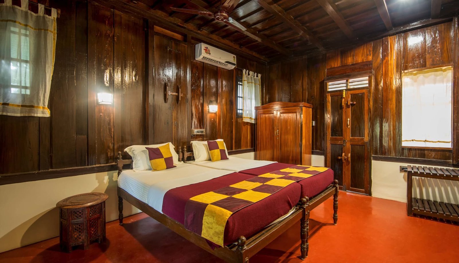 A twin-bedded room with wood-panelled walls and a polished red-oxide floor