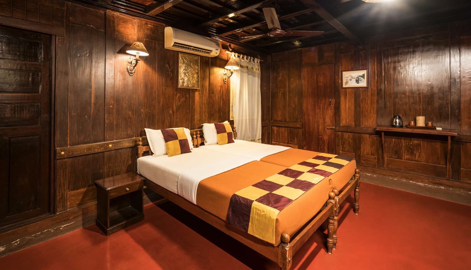 A wood-panelled room inside the house with carved teak walls and a red-oxide floor